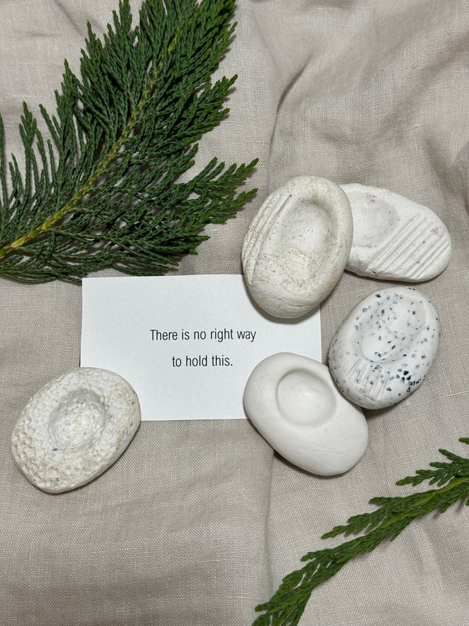 Hand-formed pale clay nest stones resting on linen beside a sprig of foliage.