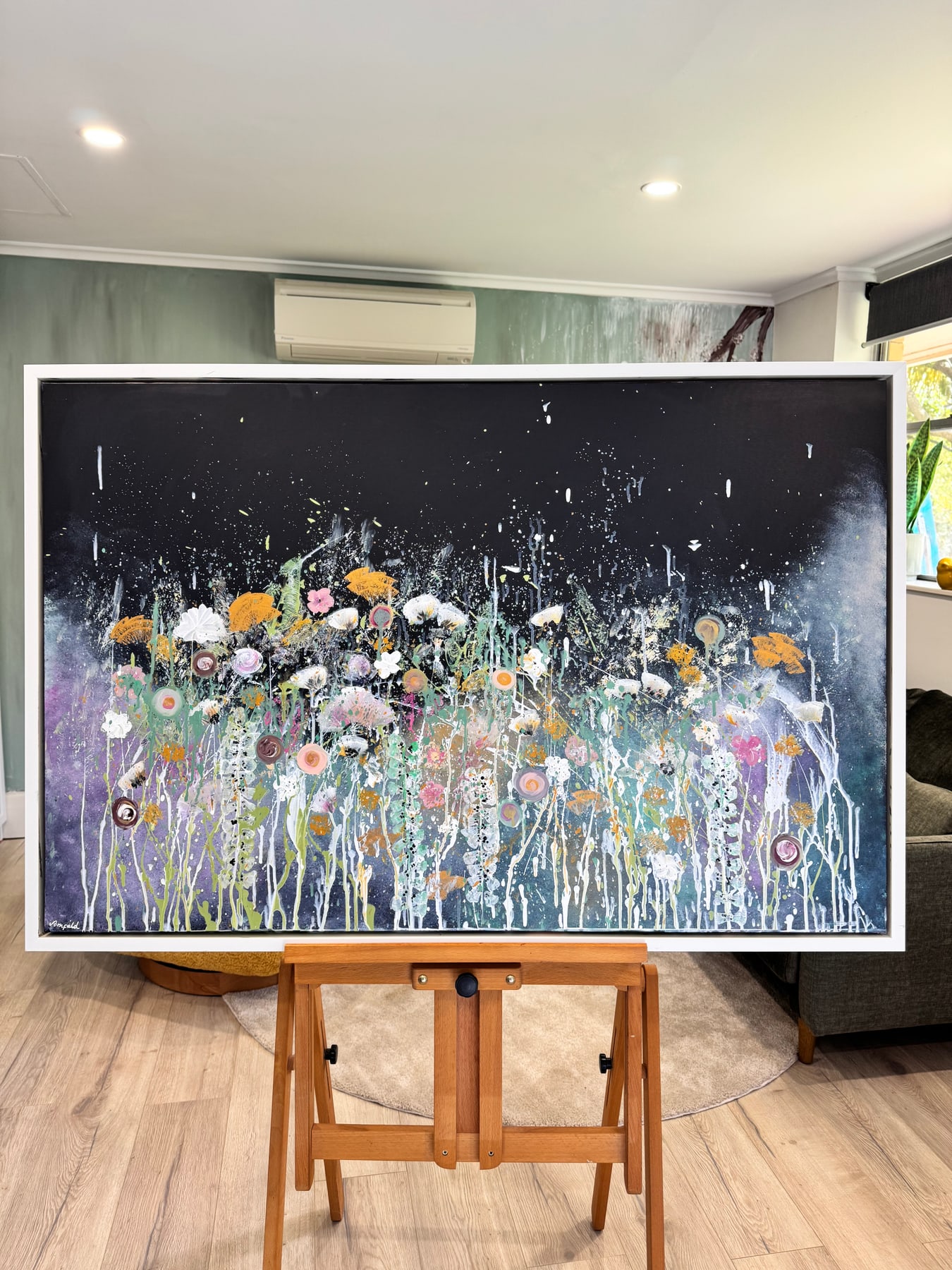 One of Niki's large flower paintings on an easel in a living room, showing the real scale of the work.